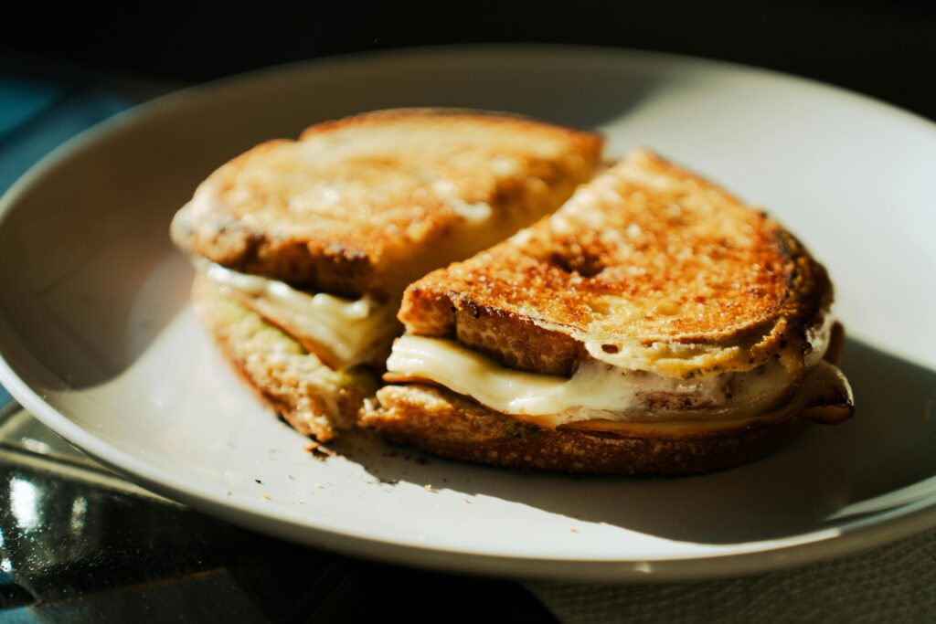 Savory grilled cheese sandwich with melted cheese on a white plate, warm lighting.